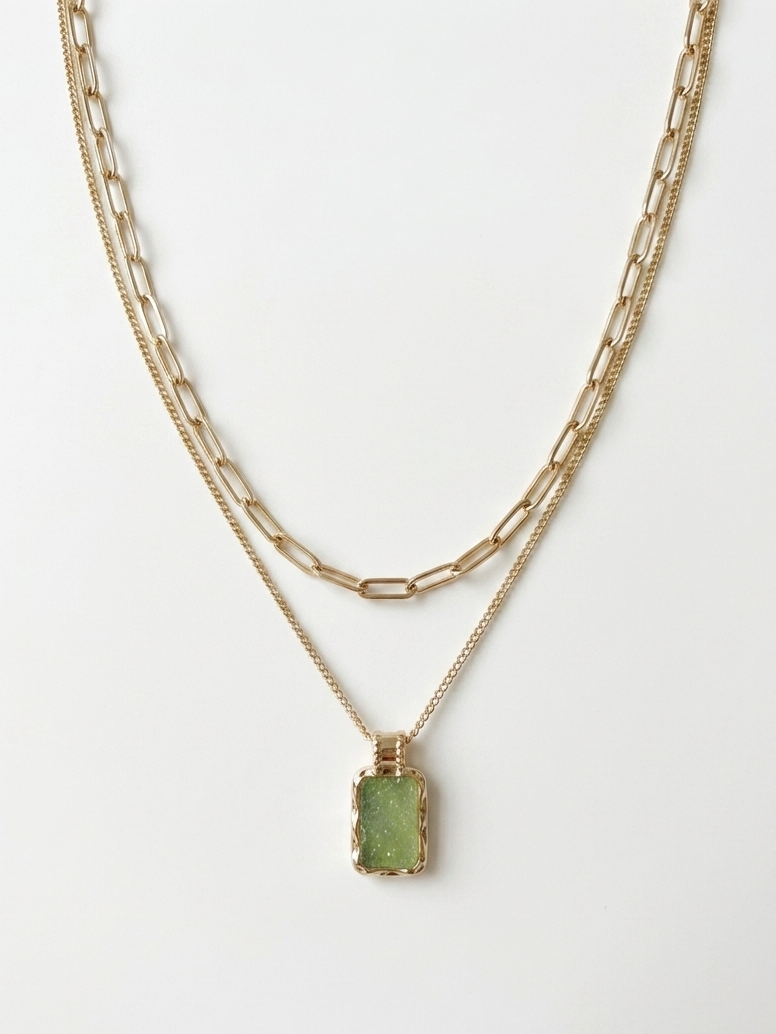 Gold layered necklace featuring a paperclip chain and light green rectangular druzy-inspired pendant on a white display.