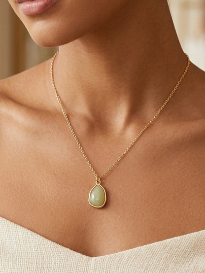 Woman wearing a gold necklace with a green pendant in a softly blurred indoor setting