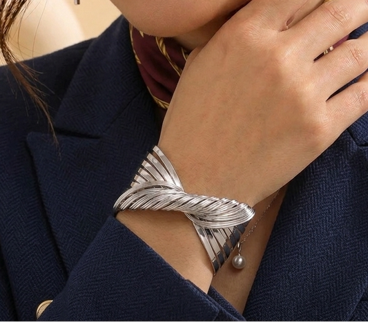 a woman wearing a twisted wrap bracelet by lumina manor on her wrist, paired with a navy blazer and a burgundy scarf.
