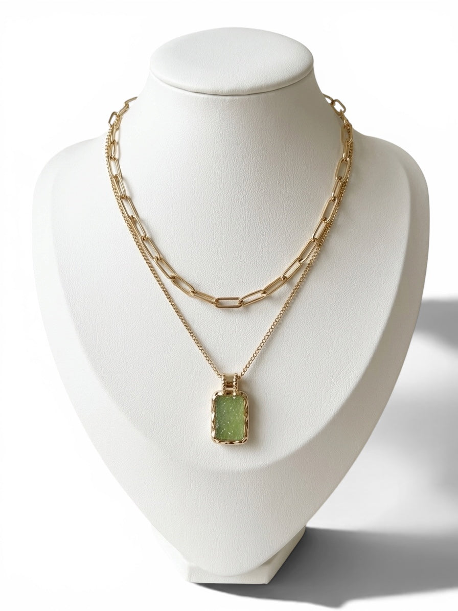 Gold layered necklace featuring a paperclip chain and light green rectangular druzy-inspired pendant on a white display.